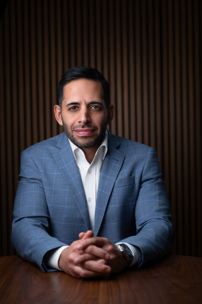 Nicholas Mukhtar seated at a desk in a blue plaid blazer